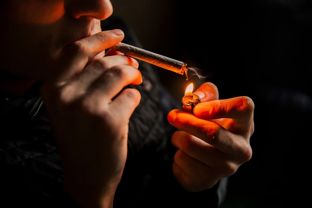 Iemand steekt een joint aan met een aansteker, ter illustratie van kush.