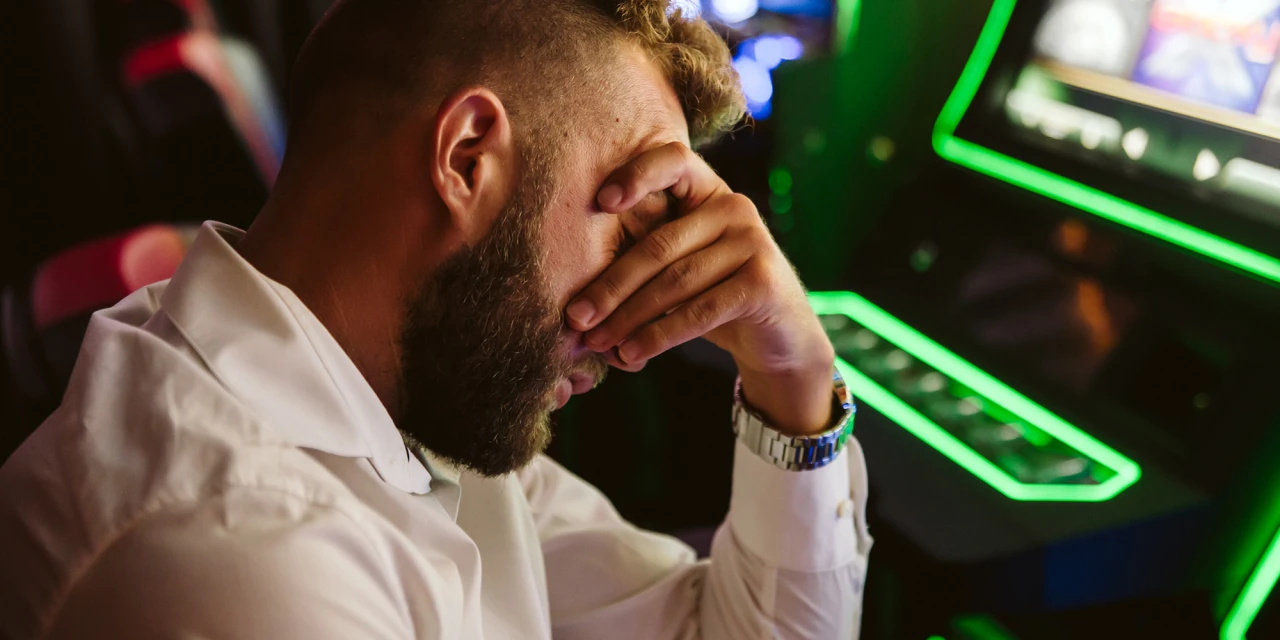 Man met hand voor gezicht bij gokautomaat toont wanhoop door gokverslaving.