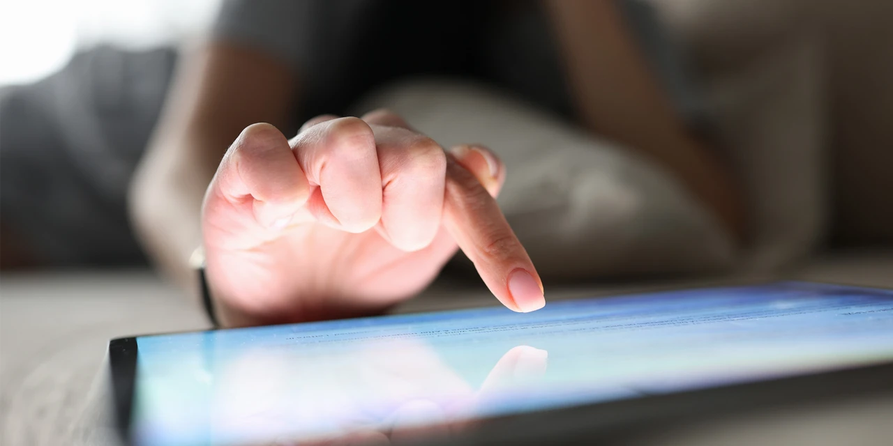 Hand tikt op tablet scherm als symbool voor internetverslaving thuis op de bank.