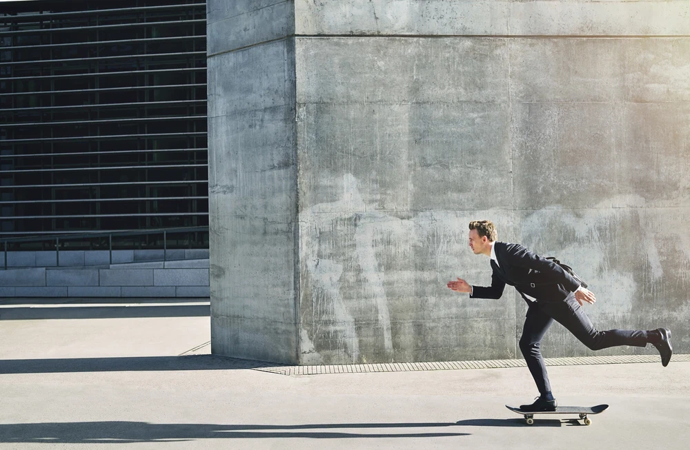Man in pak op skateboard lijkt te rennen langs gebouwen van beton.