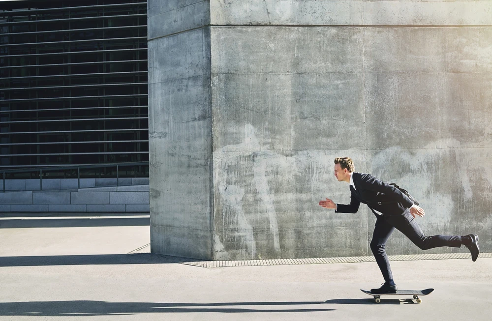 rennende-man-in-pak Man in pak op skateboard lijkt te rennen langs gebouwen van beton.