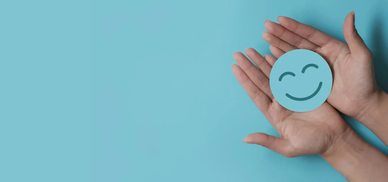 smiley-in-handen In de handen van een vrouw ligt een blauwe smiley op een blauwe achtergrond.