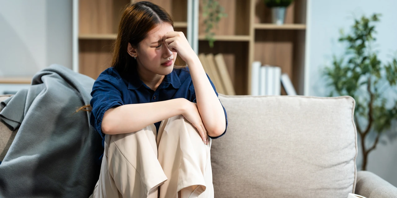 Vrouw zit somber op de bank met hand op voorhoofd, mogelijk worstelend met bipolaire stoornis.