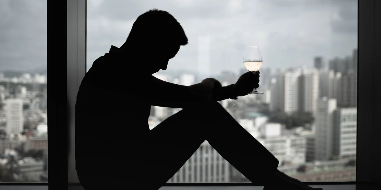Silhouet van persoon met glas alcohol bij raam in stad.