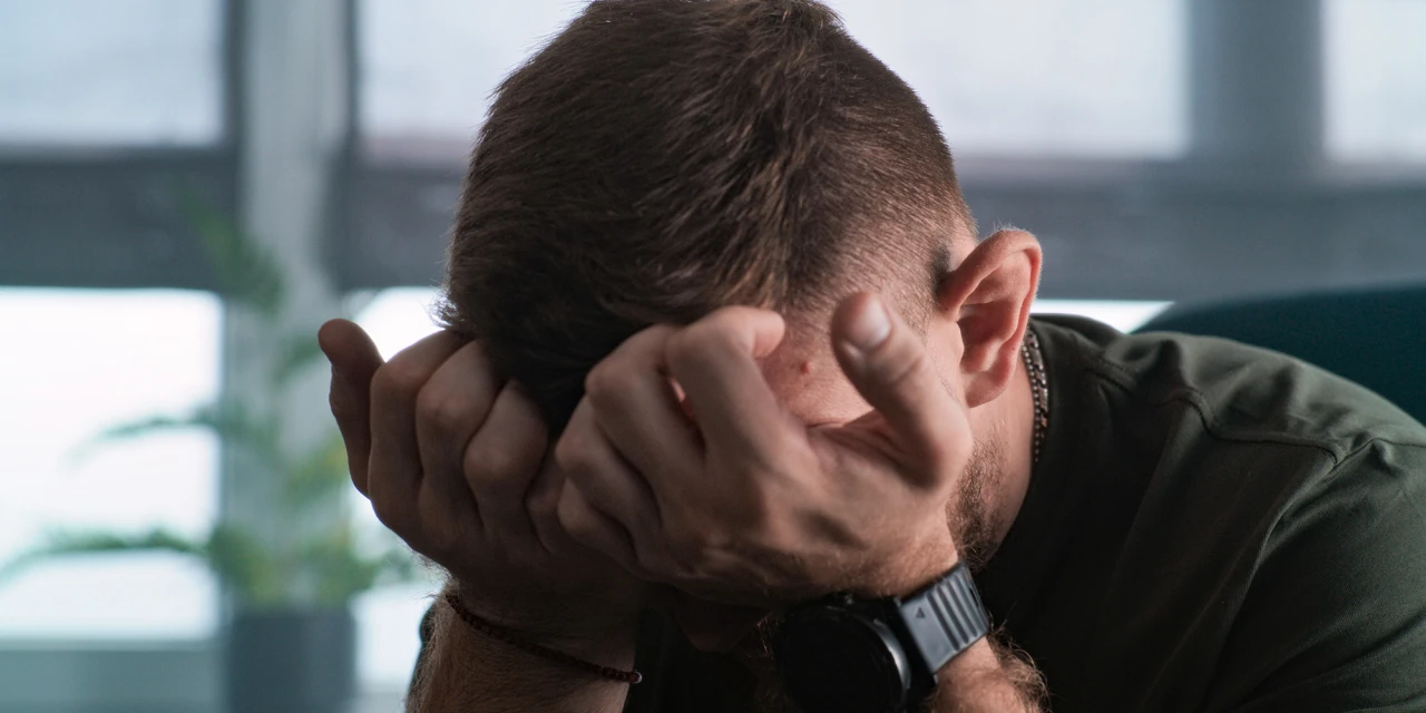 Man met handen voor gezicht op werkplek, teken van stress en mentale druk.