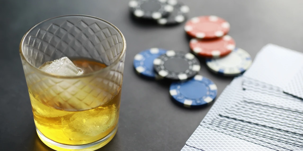 Glas whisky met ijs, pokerfiches en kaarten op tafel, combinatie van gokken en alcohol.