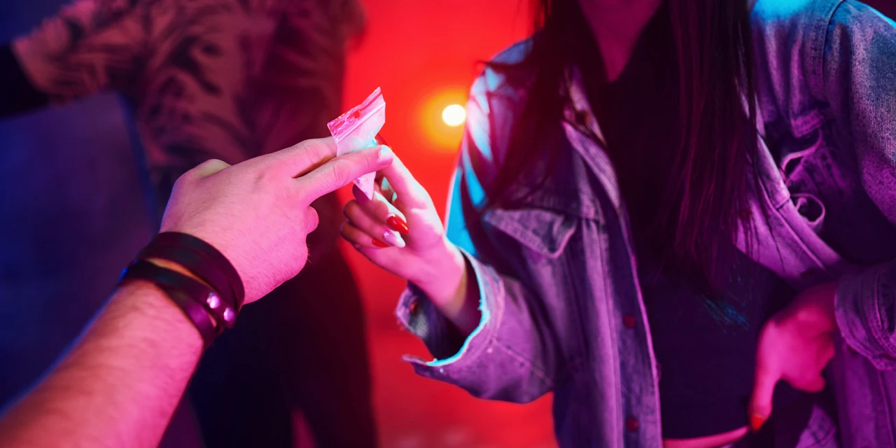 Doorgeven van drugszakje tijdens feest met gekleurde verlichting.