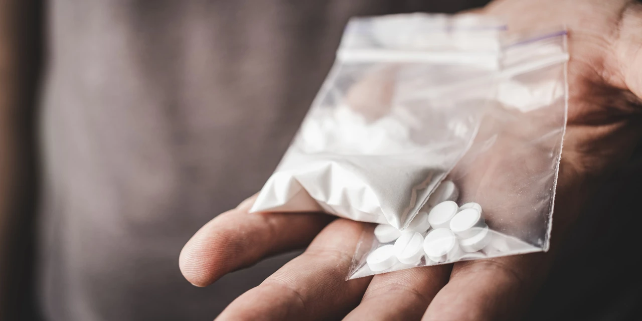 Hand met zakje wit poeder en pillen, verwijzing naar amfetaminegebruik.