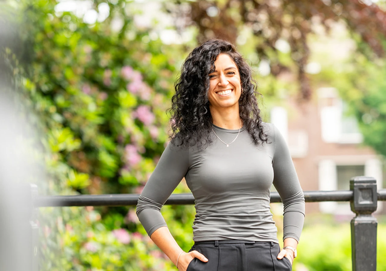 Mirjam-teamlid-Connection-SGGZ Mirjam, lid van het team van Connection SGGZ, staat vriendelijk lachend voor een hek.