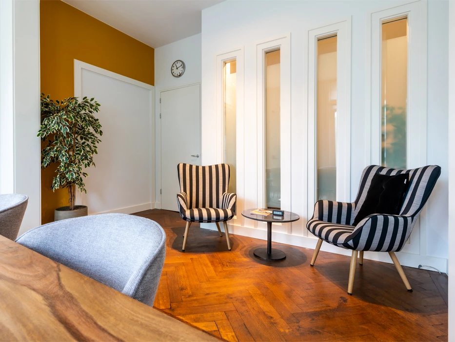 afkickkliniek-fazantlaan-gestreepte-stoelen Kamer van polikinische verslavingszorg Eindhoven, met tafel, stoelen, 2 fauteuils en salontafel.