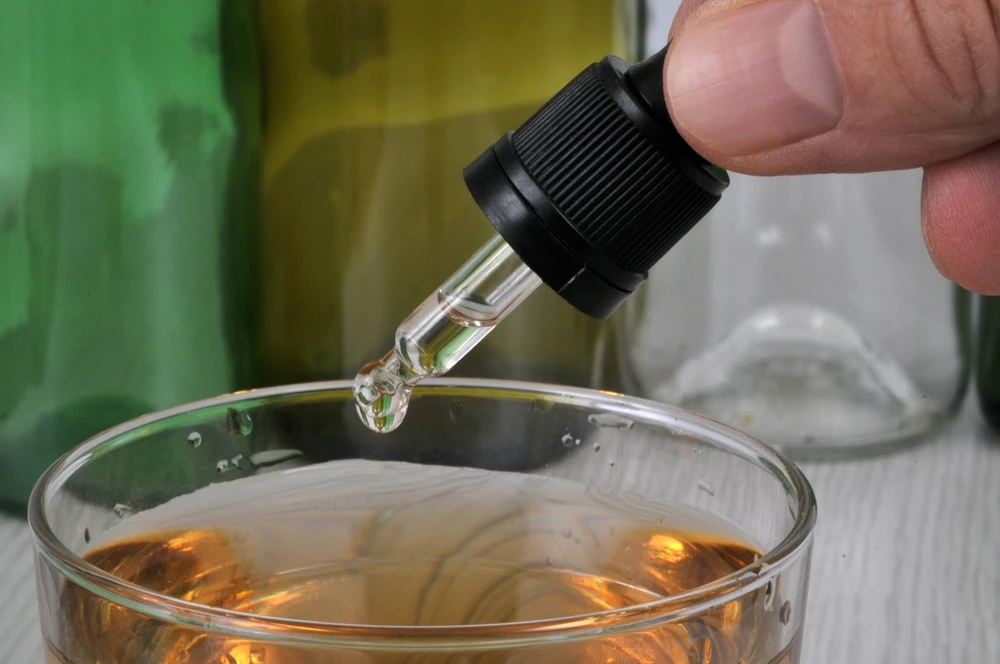 Buisje met GHB met een druppel die elk moment in een glas kan vallen; illustratie bij de vraag ‘wat is GHB’.