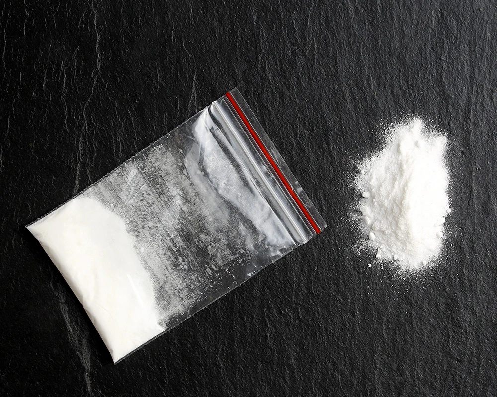 Een zakje met de witte poederdrug miauw ligt in een transparant ziplockzakje op een donkere tafel.