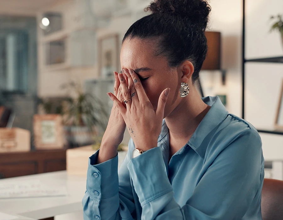 Vrouw zit op werk met hand voor gezicht, beeld van mentale overbelasting en spanning.