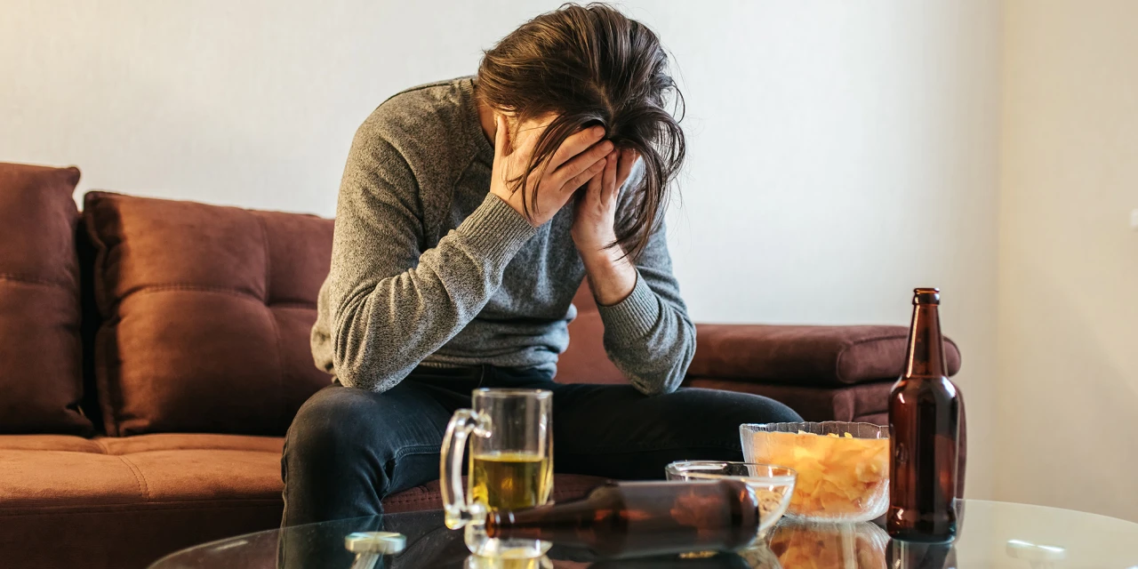 Man zit op de bank, wanhopig door afkickverschijnselen alcohol, met lege flessen om zich heen.