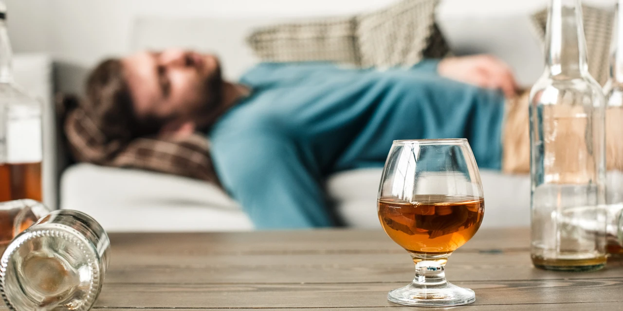 Man ligt uitgeput op bank met glas sterke drank op tafel door alcoholabusus.