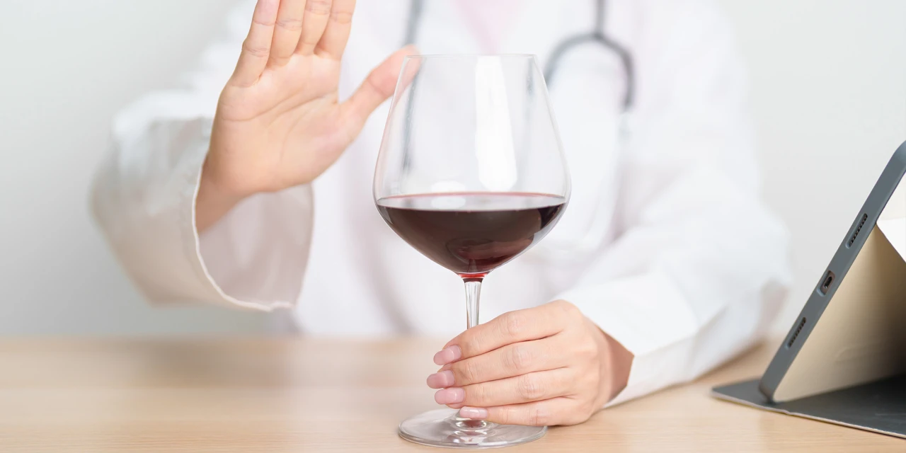 Arts houdt hand omhoog om wijnglas weg te duwen als waarschuwing voor leveraandoeningen door alcohol.