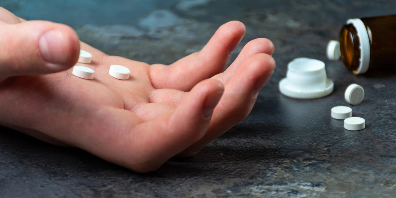 Hand met witte pillen naast een geopend medicijnflesje.