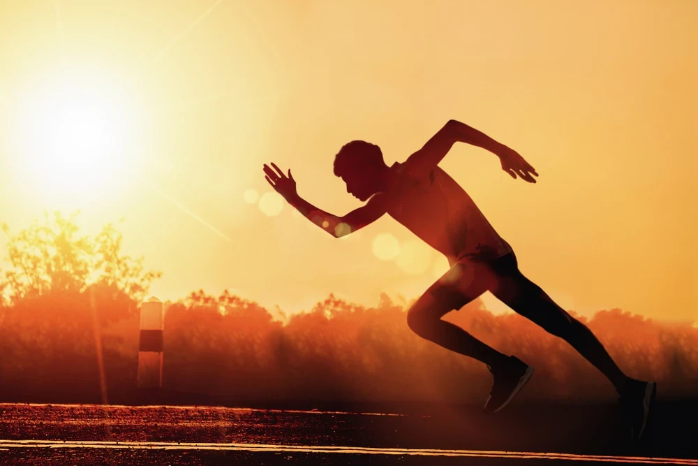 Rennende mannelijke sporter met op de achtergrond ondergaande zon.