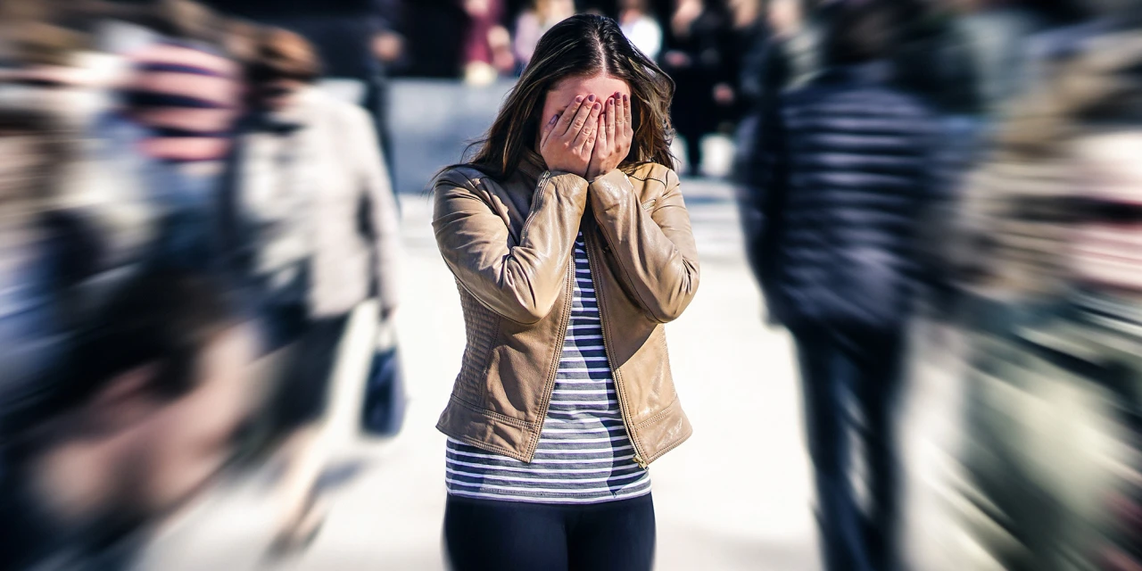 Vrouw in drukke straat met handen voor gezicht, overweldigd door depressie.
