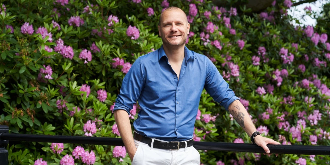 Bastiaan Meyers, medisch directeur bij Connection SGGZ, staat buiten voor een struik met roze bloemen en glimlacht.