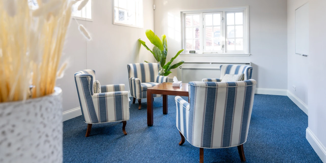 Lichte gesprekskamer met stoelen en tafel bij raam.