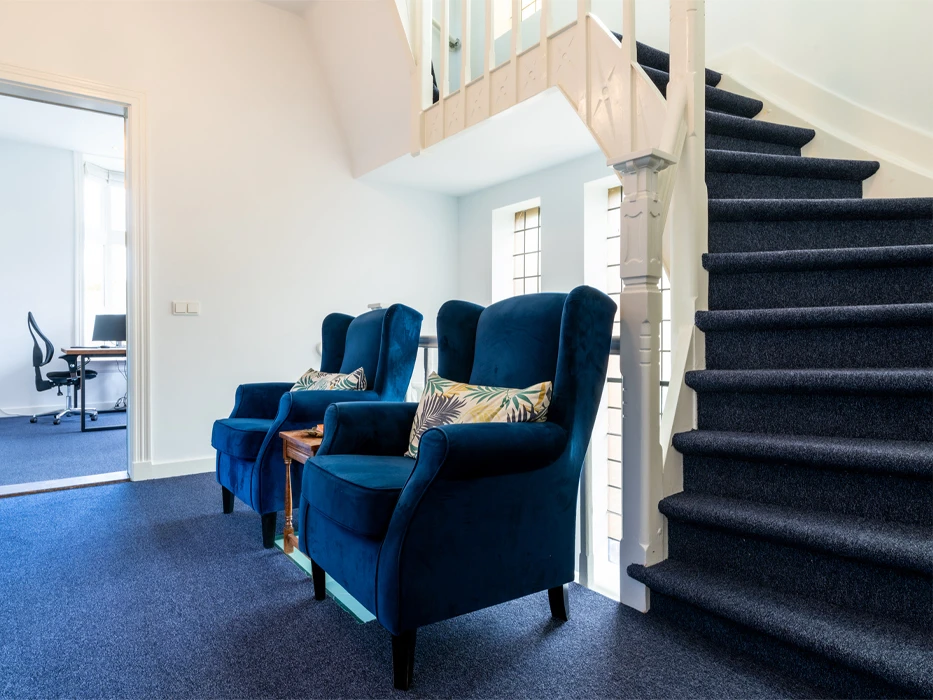 afkickkliniek-fazantlaan-hal Hal van poliklinische verslavingszorg Eindhoven, met 2 fauteuils, blauwe vloer en blauwe trap.