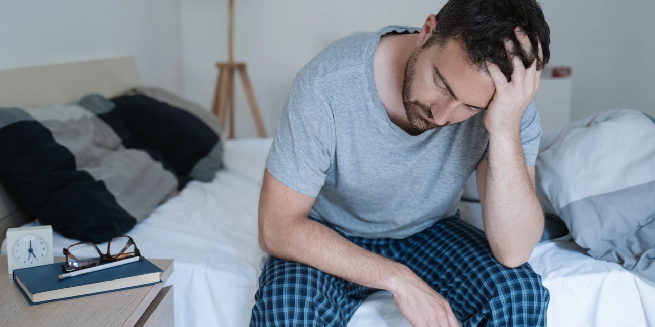 Man zit op bed met hand in haar, oogt uitgeput, beeld van PTSS-klachten.