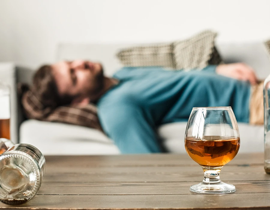 Een man ligt op de bank, terwijl de gevolgen van alcohol voor je lichaam zichtbaar worden.