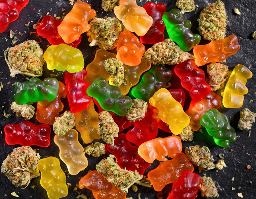 Bovenaanzicht van gummybeertjes en cannabistoppen door elkaar, ter illustratie van edibles