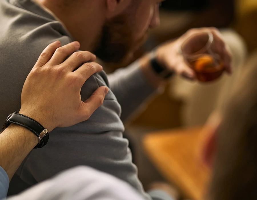 Hand op de schouder van een man met een glas whisky, ter illustratie van de ziekte van Korsakov.