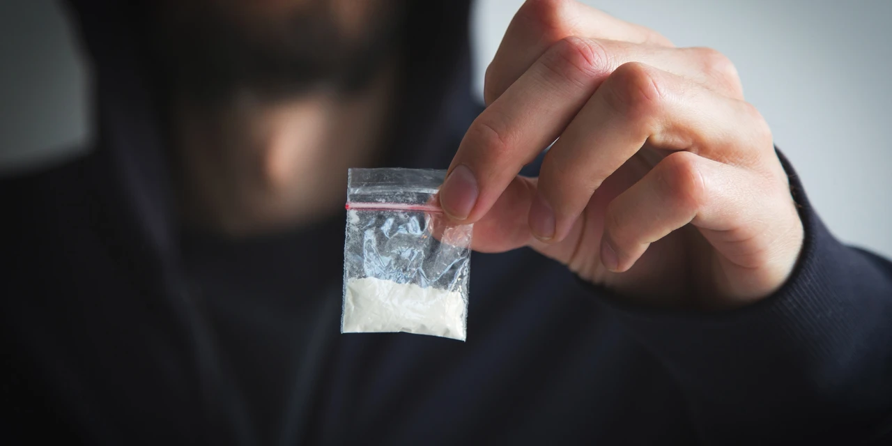 Persoon houdt zakje met wit poeder vast. Hoe kun je cocaïnegebruik herkennen?