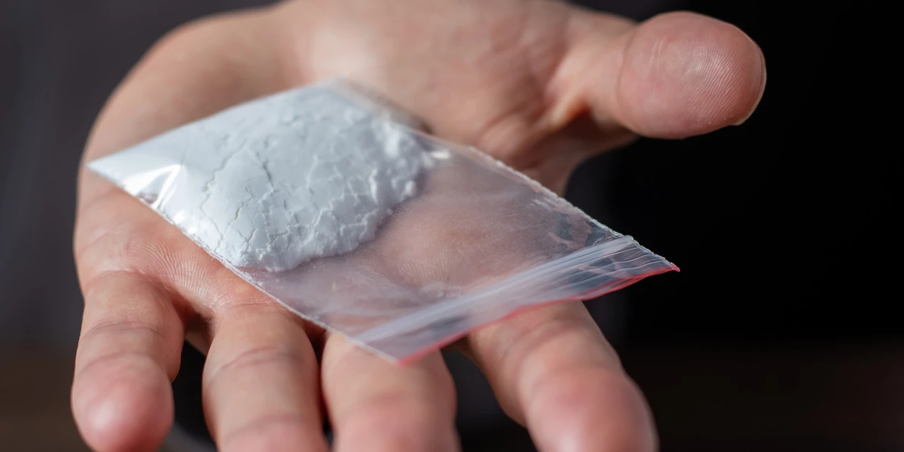 Hand met zakje wit poeder dat symbool staat voor cocaïneverslaving.