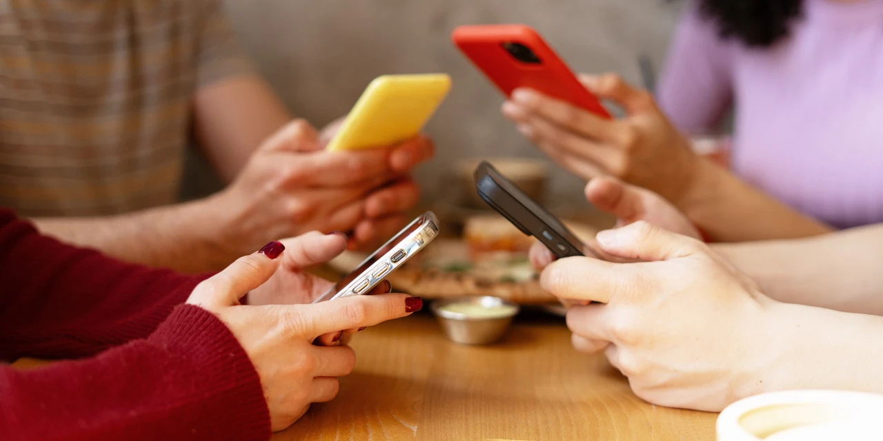Groep mensen kijkt op telefoon tijdens eten wat social media verslaving laat zien.