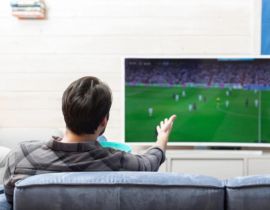 Man op bank kijkt tv en besluit te wedden op voetbal terwijl hij snacks vasthoudt.