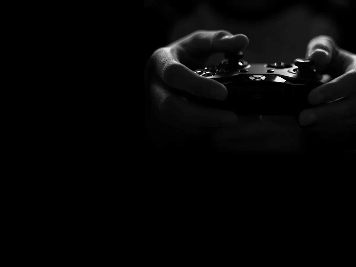 Donkere zwart-wit foto van twee handen die een gameconsole vasthouden. 