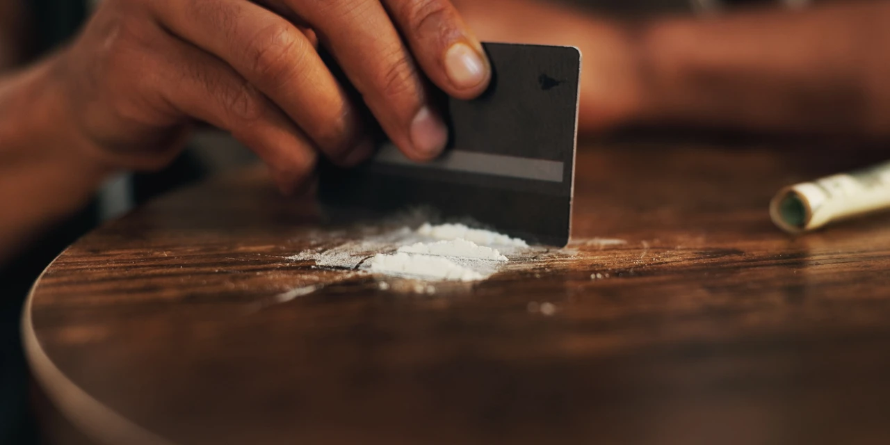 Hand met pas verdeelt wit poeder op tafel bij wat designerdrugs zijn.