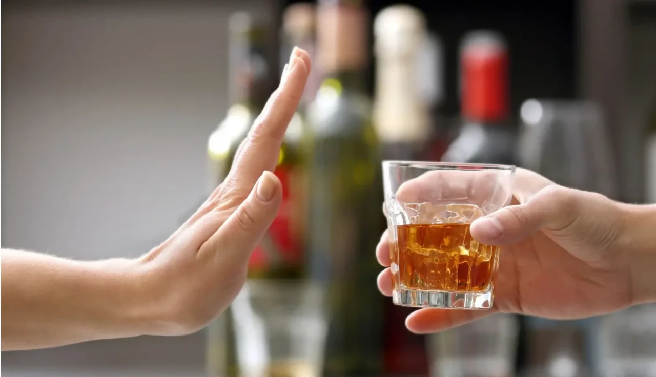 stoppen-met-alcohol-drinken Een hand met een wiskeyglas tegenover een hand die het signaal geeft om te stoppen met drinken.