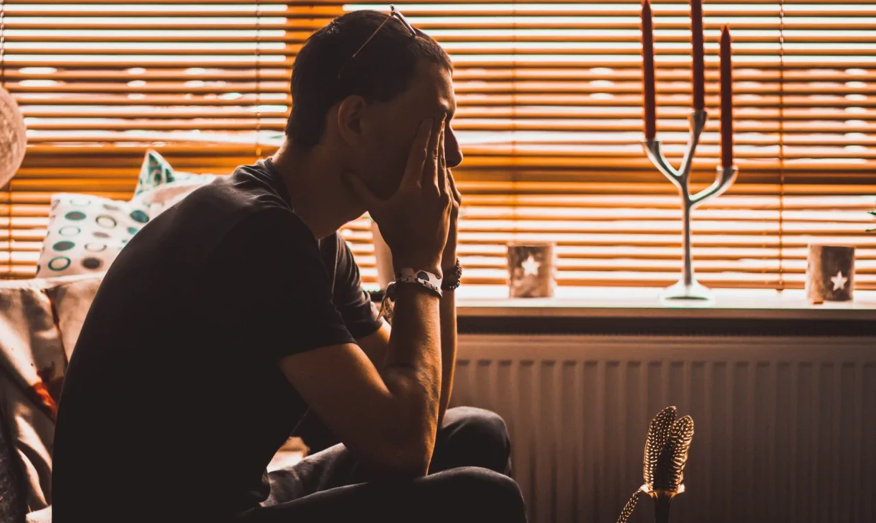 man-met-afkickverschijnselen-wiet Man heeft last van de afkickverschijnelen van wiet en zit met de handen voor de ogen in een kamer.