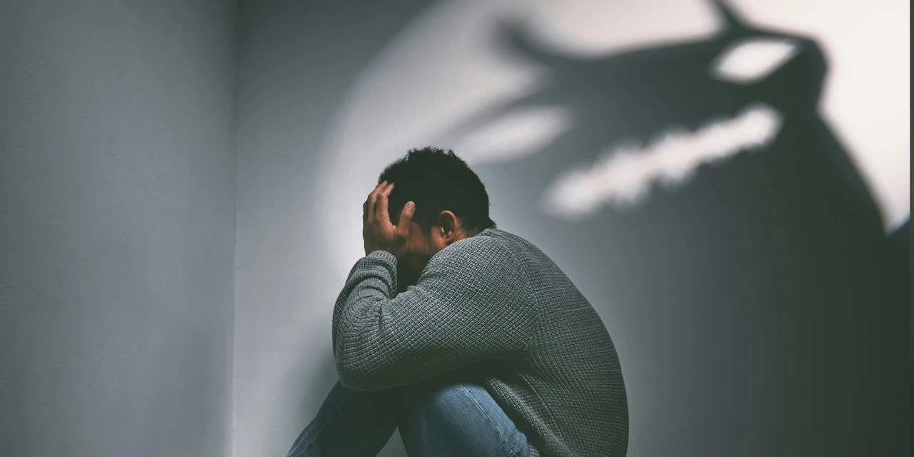 Man zit ineengedoken met hoofd in handen, verbeelding van trauma.