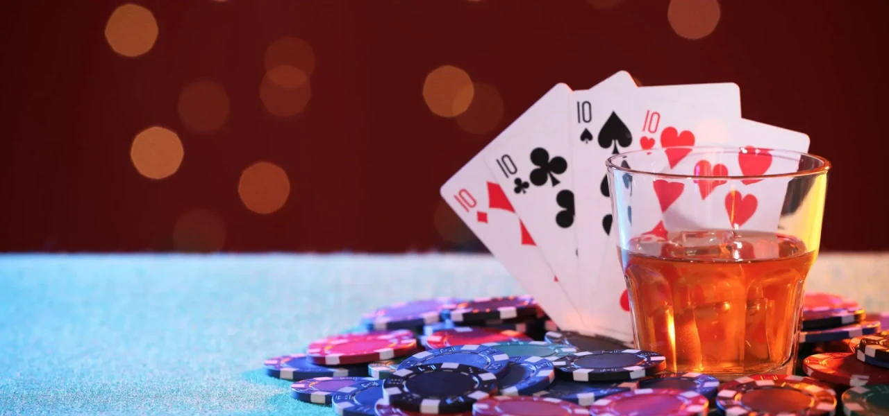 Op een tafel staat een glas alcohol met daarachter gokkaarten en gokfiches.