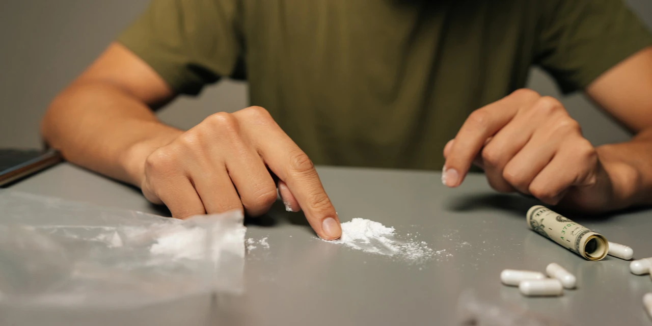 Persoon bereidt drugs op tafel, mogelijk door verslavingsgevoeligheid.