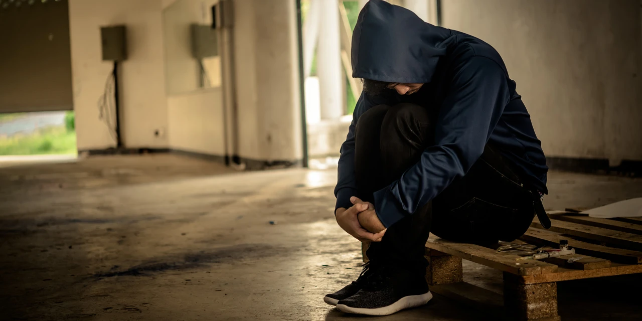 Persoon zit ineen gedoken in lege ruimte na drugsgebruik.
