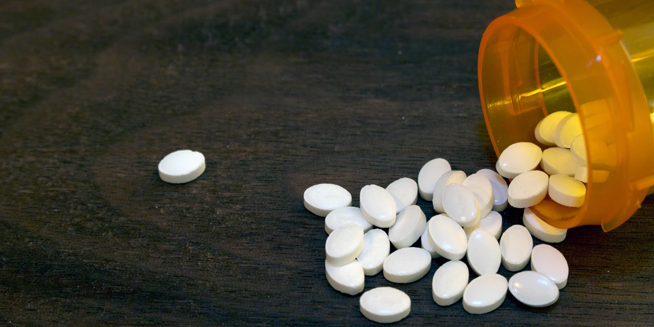 Witte tabletten uit pillendoos op tafel, beeld van medicatie en opiatengebruik.