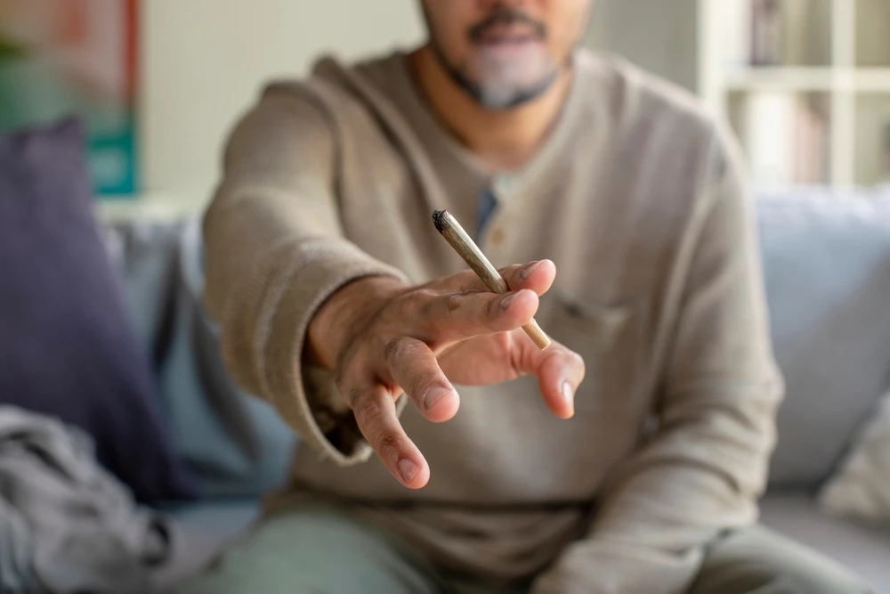 Man houdt een brandende joint vast, wat kan wijzen op cannabisverslaving.