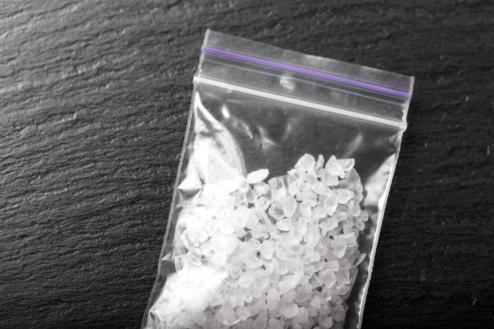 Doorzichtig zakje met witte kristallen van de drug miauw miauw op donkere ondergrond.