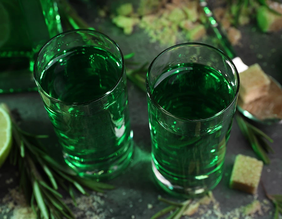 Twee glazen groene absint met suikerklontjes en kruiden.