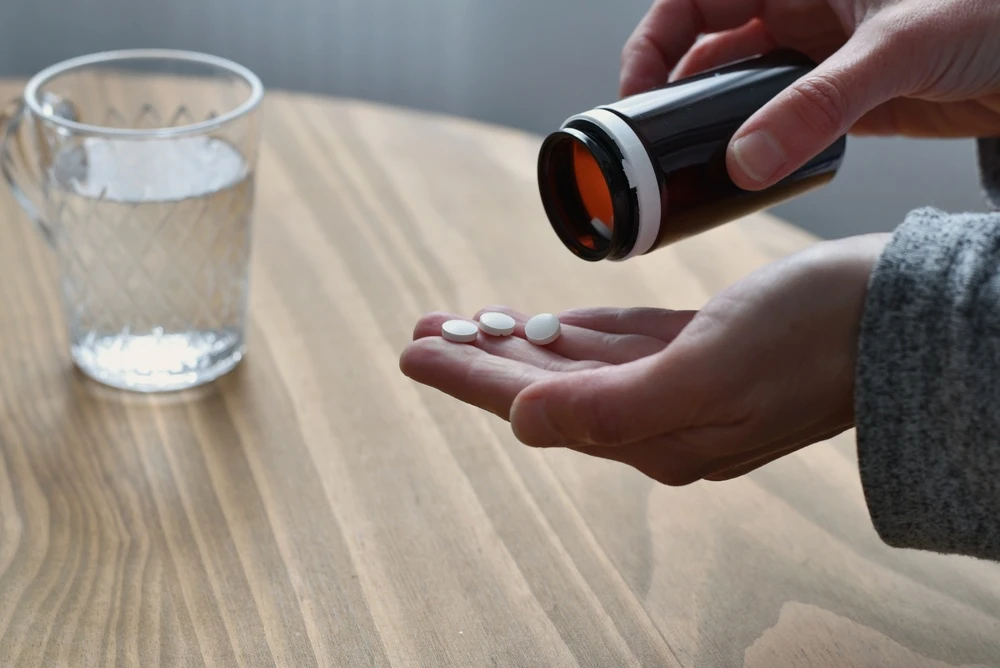 Witte tabletten uit een potje in een hand naast een glas water, ter illustratie van nitazenen.