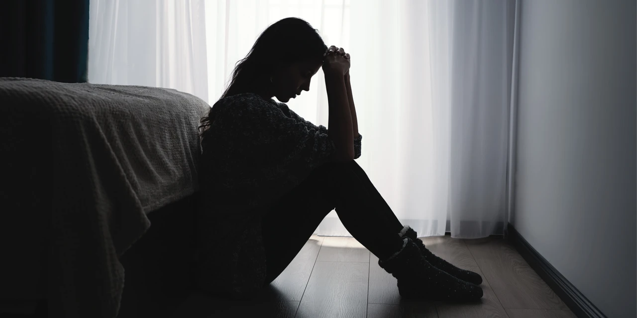 Vrouw zit somber op de vloer bij raam en denkt na over wanneer je alcoholist bent.