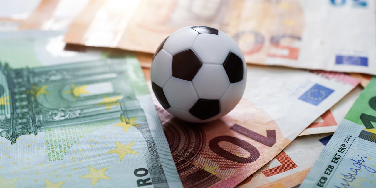 Miniatuur voetbal ligt op stapel eurobiljetten als symbool van wedden op voetbal.