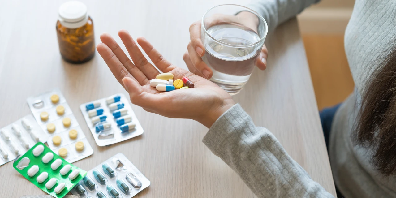 Persoon met glas water en pillen in hand, mogelijk verslaafd aan pijnstillers.
